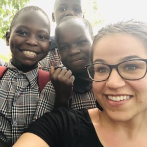 A woman in glasses and three young children smile at the camera